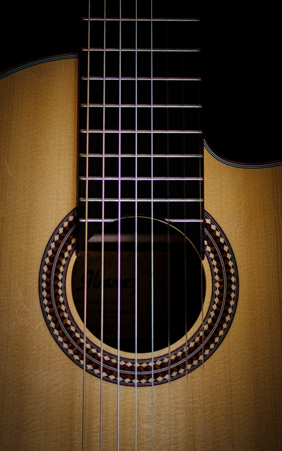 Nahaufnahme einer klassischen Akustikgitarre mit Fokus auf Saiten und dekorativer Schallloch-Rosette